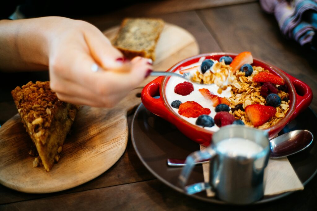 Close-up of a breakfast setting with granola, fresh berries, and a slice of cake.